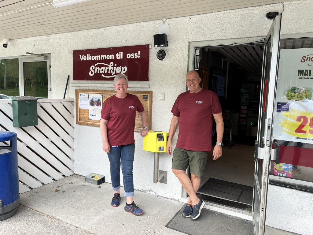 Ansatte ved Snarkjøp Herefoss smiler ved siden av den gule adgangsterminalen.