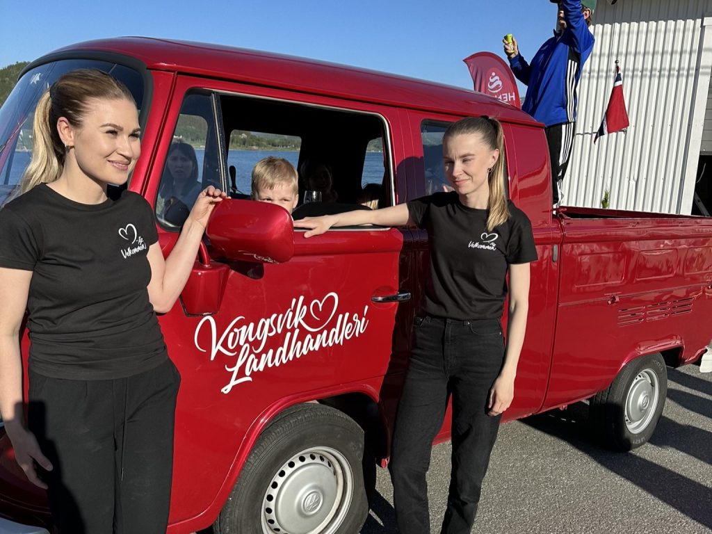 Butikkdriverne smiler forran en bil med logoen til butikken.