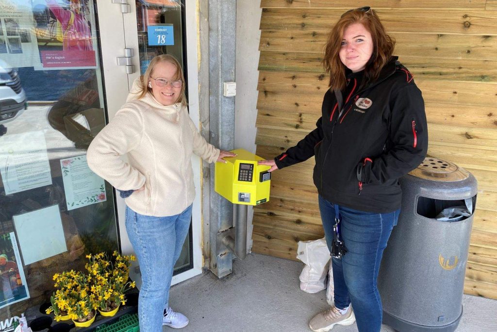 daglig leder i Nærbutikken Korshamn, Lindy Cecilie Sikveland Kaldestad står ved siden av den gule adgangsterminalen med en representant fra butikken.