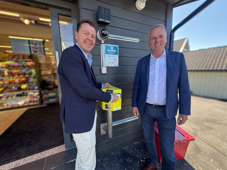 Snorre Corneliussen og Hans Olav Bakås står ved siden av den gule adgangsterminalen ved en butikk med RMA-Teknologi.